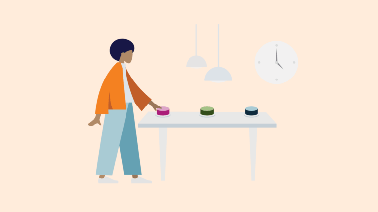 Person steht an einem Tisch und drückt einen farbigen Knopf; auf dem Tisch liegen weitere Knöpfe, im Hintergrund hängen Lampen und eine Uhr.